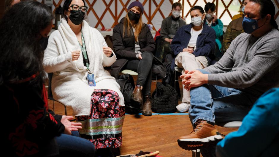 Group of people sitting inside of the UBC Farm yurt. Three are centered and having a seated conversation.