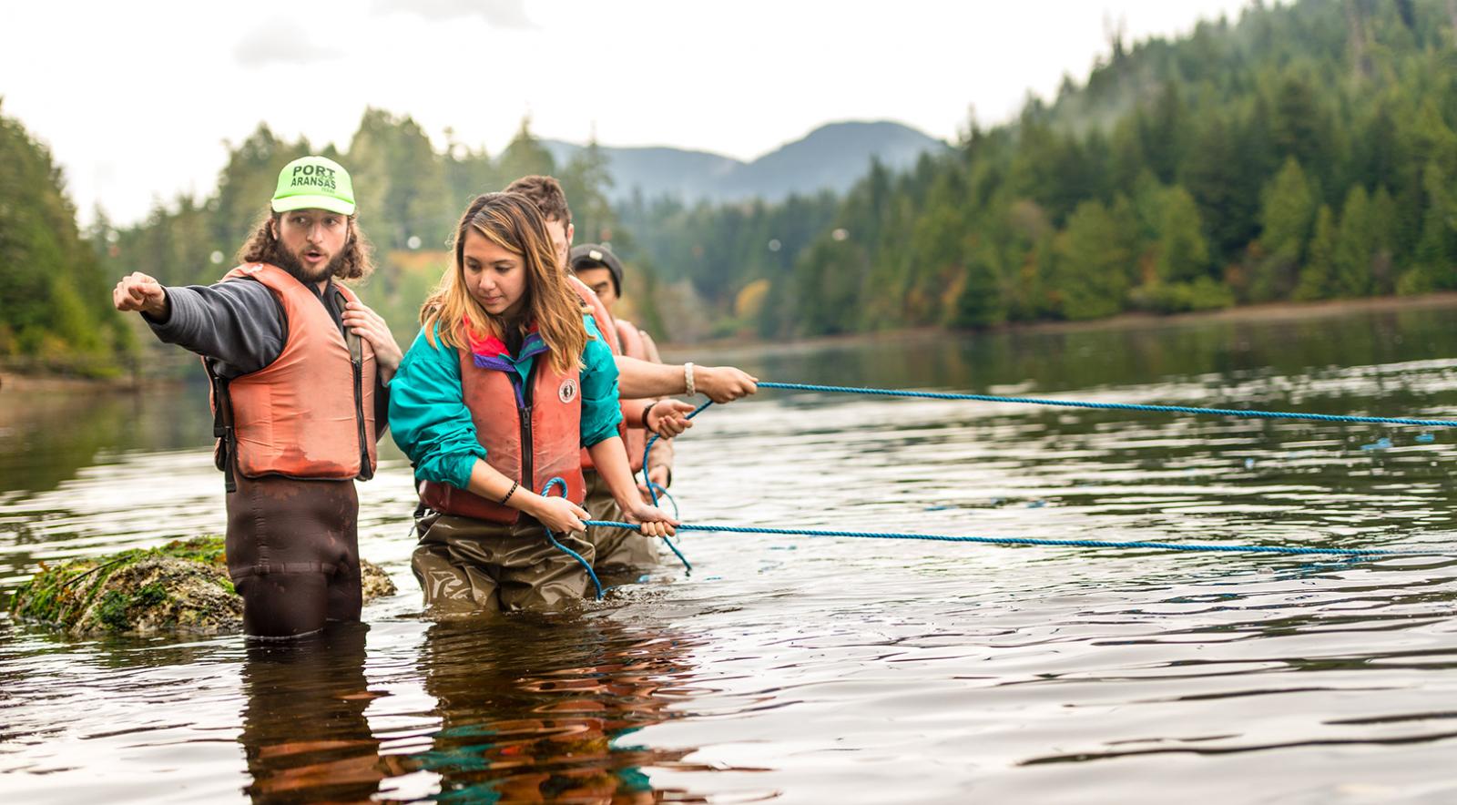 Four students in waders conducting ocean research in the shore